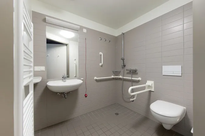 Barrierefreies Badezimmer mit Waschbecken, Haltegriffen und wandhängendem WC.