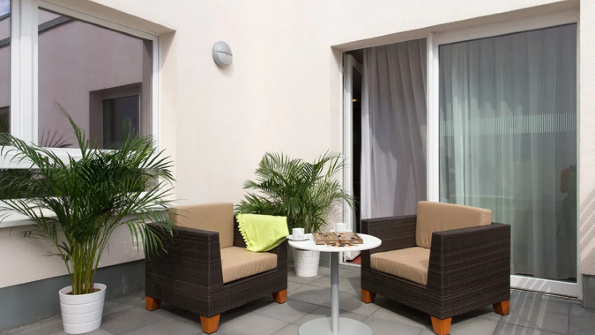 Zwei Korbsessel und ein Tisch auf modernem Balkon, mit Topfpflanzen und Vorhängen.